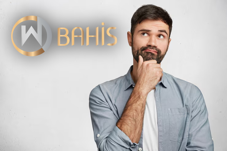 Sakallı ve bıyıklı bir adam, açık mavi bir gömlek giymiş, eli çenesinde düşünceli bir şekilde duruyor. Yanında beyaz zemin üzerinde WBAHİS yazan altın ve gümüş renkli bir logo "Neden WBahis'e Üye Oldum?" sorusunu ima etmektedir.